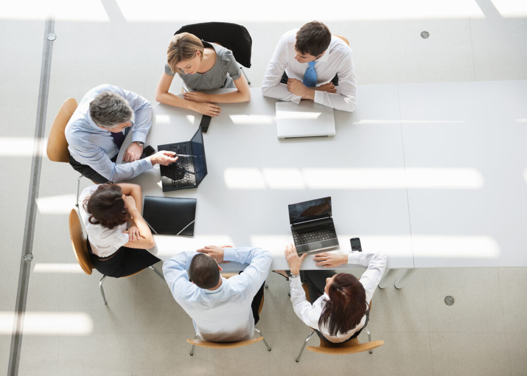 Group of people collaborating with laptops around a table.